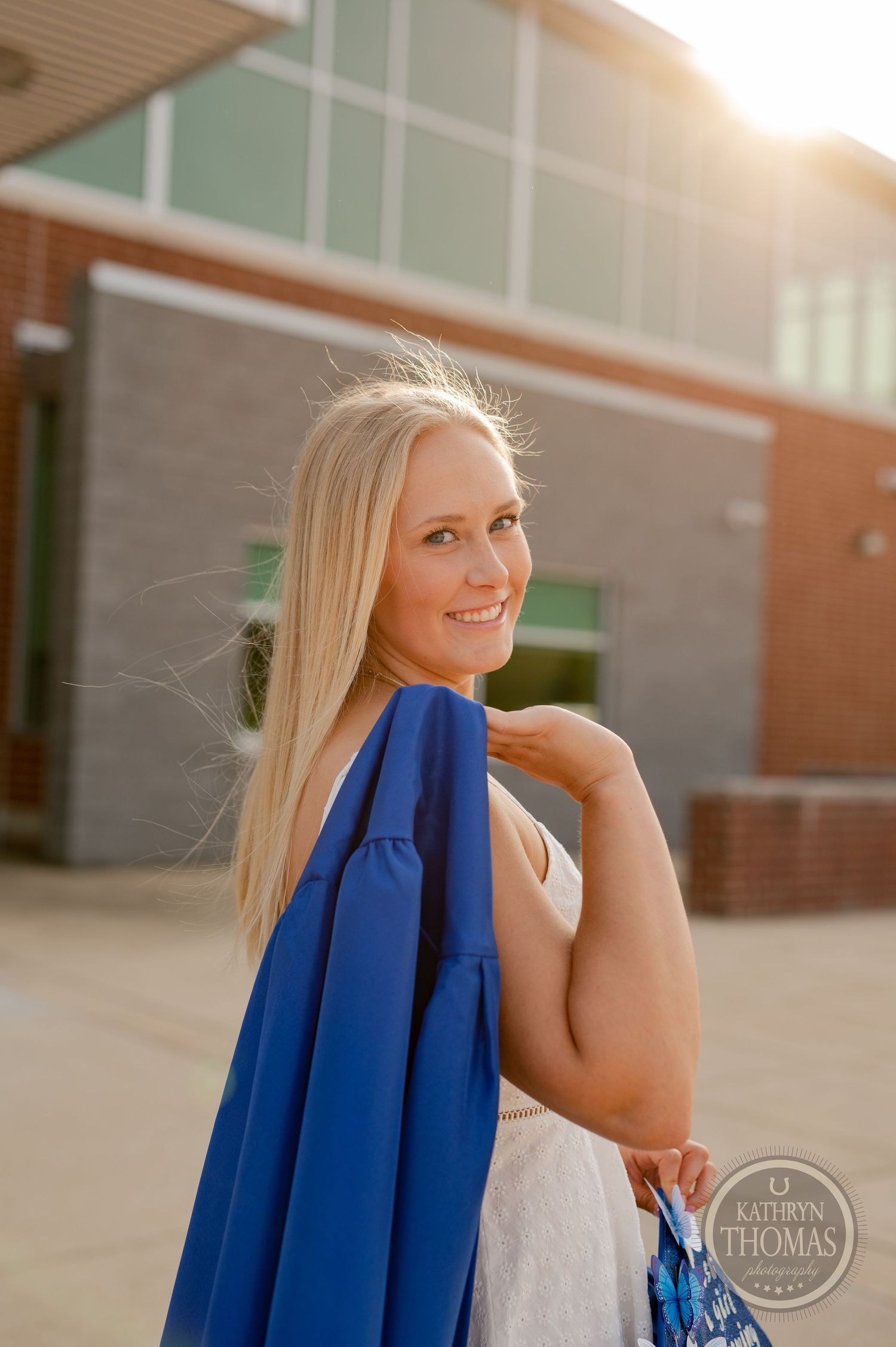 Sunset graduation photo featuring blue gown against modern school architecture.
