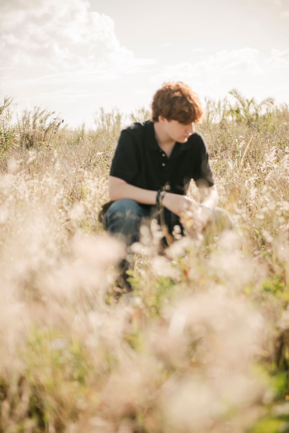 Senior sits among tall grass in a dreamy, sunlit field.