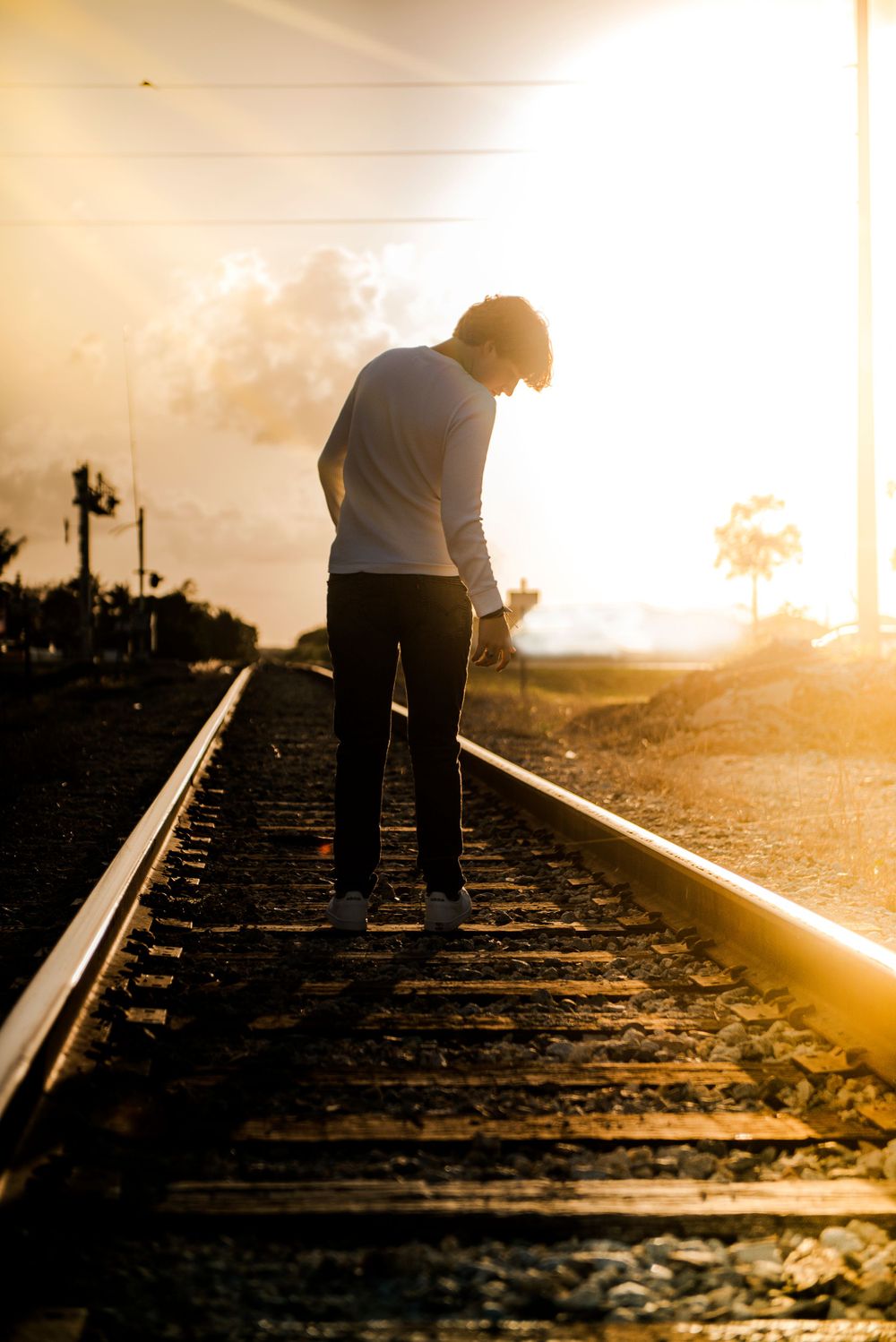 Senior standing on train tracks during golden sunset.