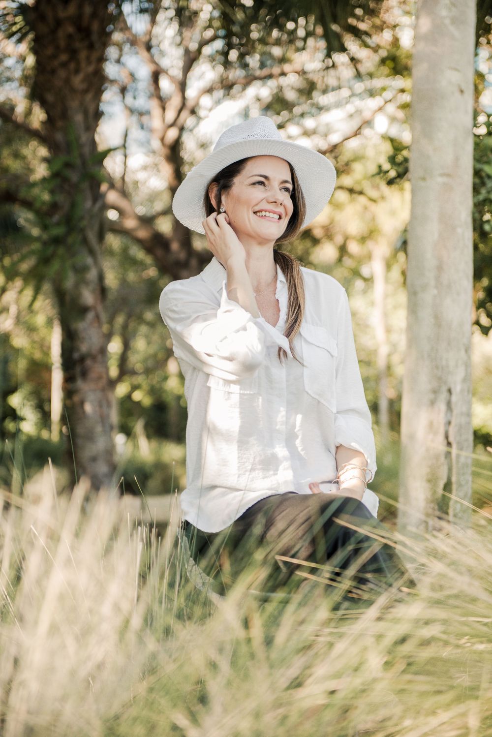 Yoga instructor sits outdoors among tall grasses on a sunny day in a natural setting.