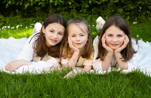 Three young friends lying on a white blanket in grass with daisies on a sunny day.