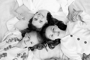 Three children lying down with heads together in black and white artistic portrait.