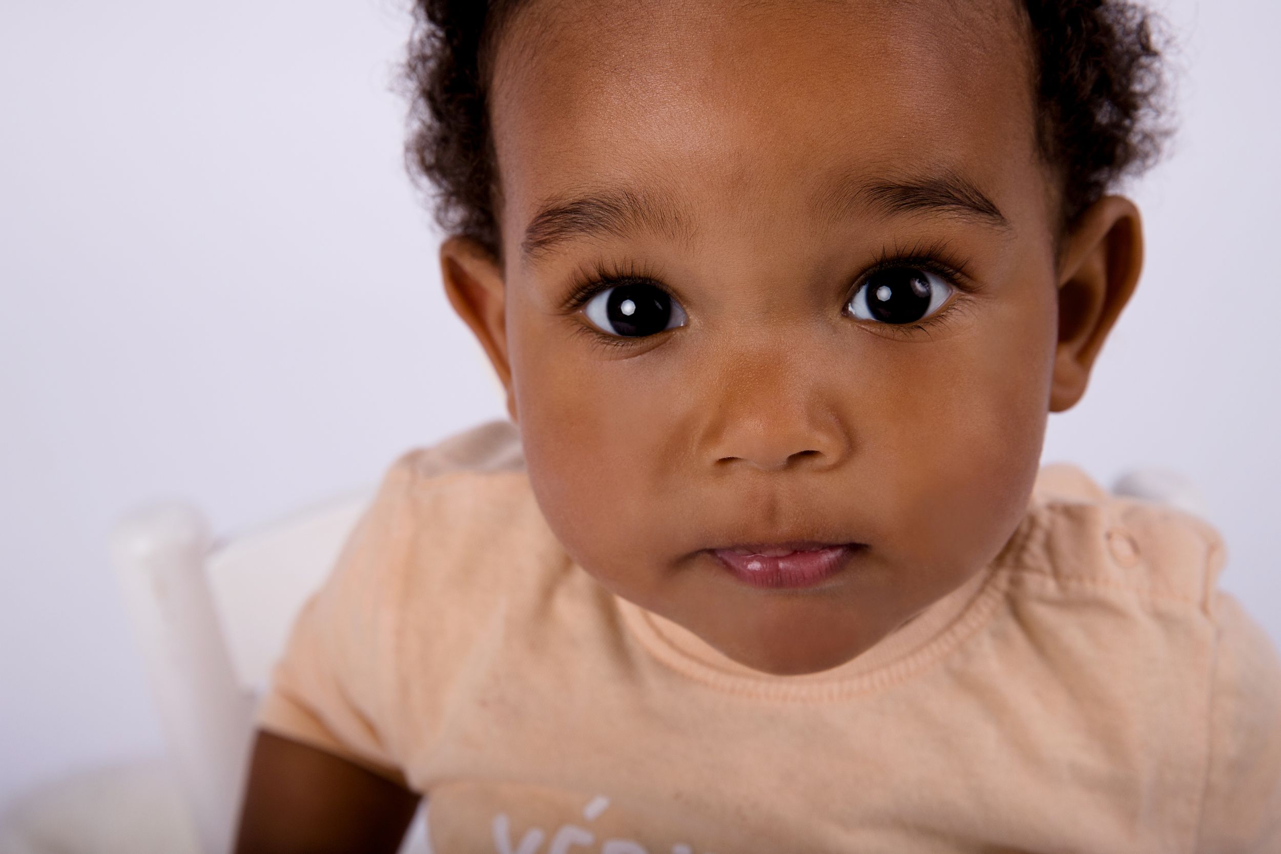 Close-up portrait of a young child in a beige shirt against white background.
