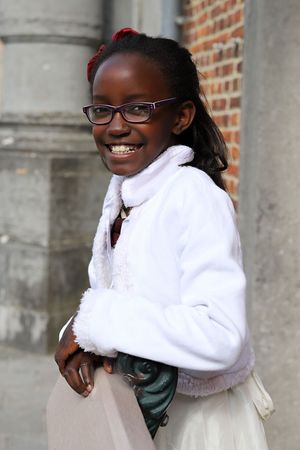 Portrait against brick wall featuring white winter coat and glasses with bright smile.