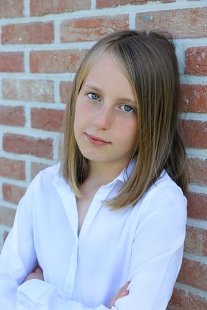 Studio portrait against a brick wall wearing a white button-down shirt.