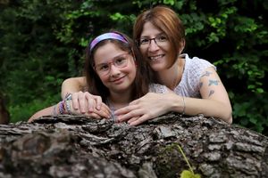 Two people leaning on rustic log in woodland setting during photo session.