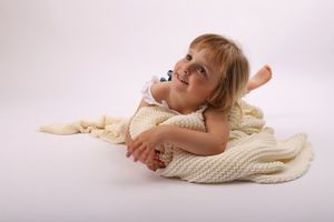 Young child lying on cream knit blanket against white background.
