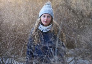 Winter portrait of someone in a knit hat and scarf surrounded by dried grass and brush.