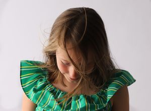 Artistic portrait featuring a green striped ruffle dress with downward gazing pose against light background.