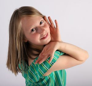 Playful studio portrait with green striped dress and cheerful pose against white backdrop.