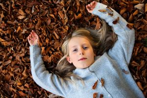 Overhead view of person lying in fallen autumn leaves wearing grey sweater.