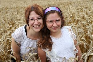 Two people in white lace tops pose together in a golden wheat field on a sunny day.