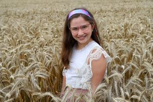 Person wearing white lace top and purple headband poses in wheat field.