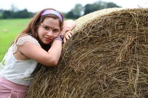 Person in white lace top resting against large round hay bale in rural field.