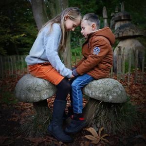 Two people sitting close together on stone mushroom sculptures in autumn garden setting.