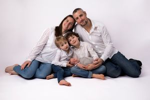 Family in matching white and blue outfits pose together on white background for portrait.