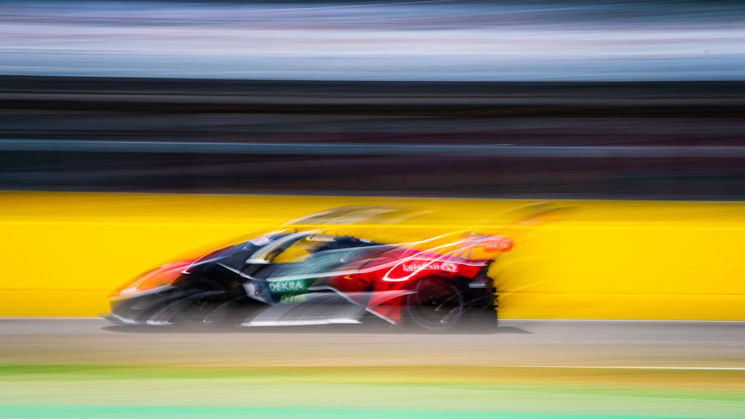 Motion-blurred racing cars create abstract streaks of color on a racetrack.