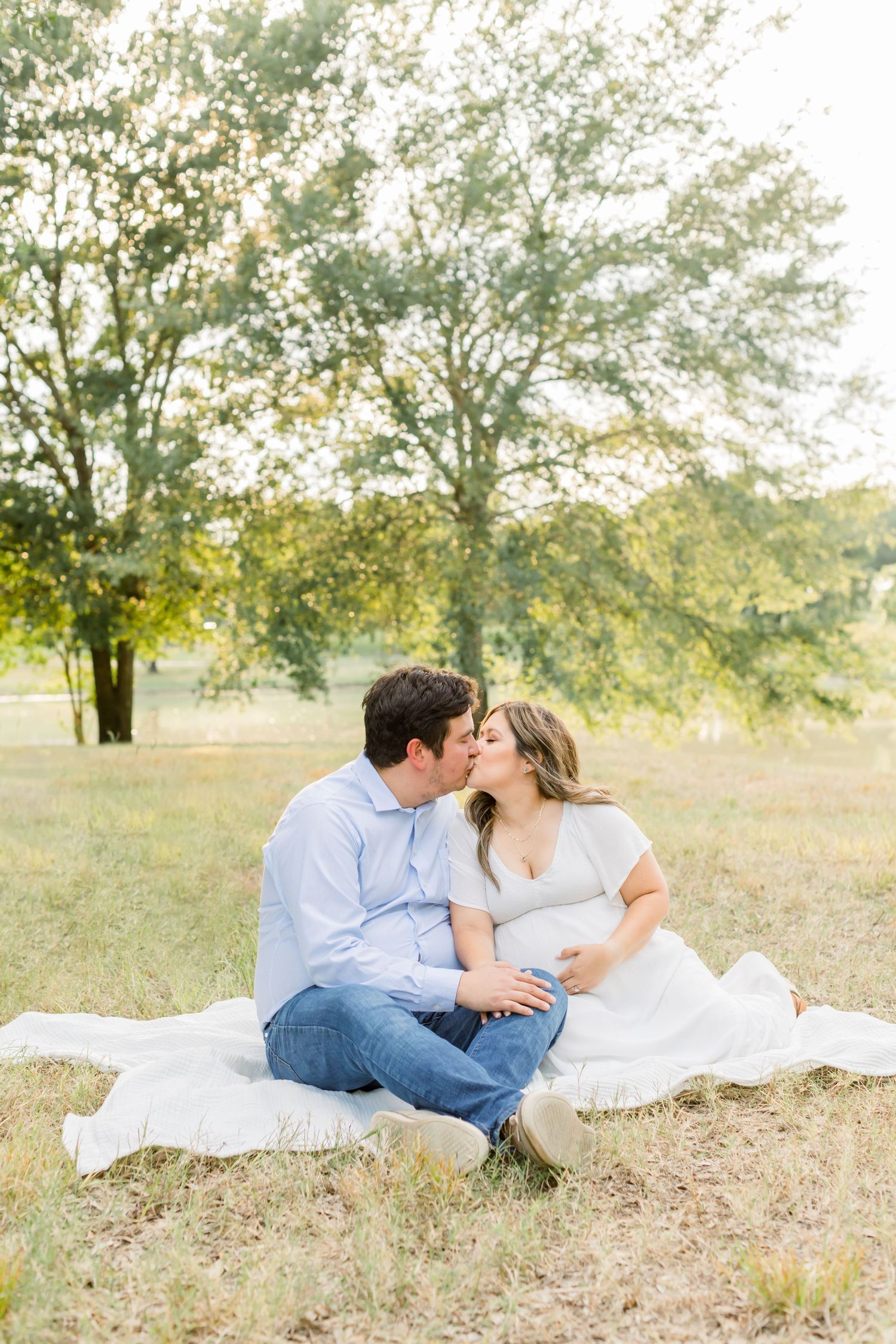Loving couple shares an intimate moment while sitting on a blanket in a grassy field at sunset.