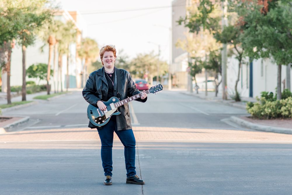 senior session girl holding electric guitar in the middle of the street downtown Winter Haven, Florida