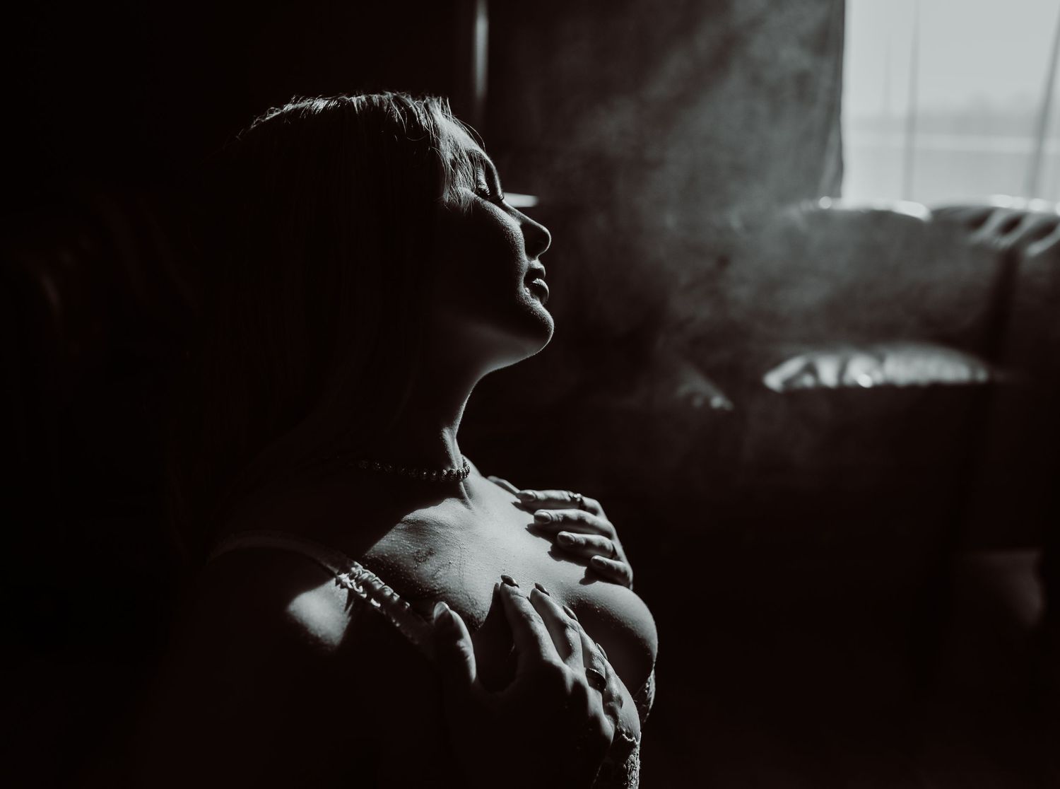 A silhouetted figure is illuminated by dramatic window light in a moody black and white photograph.