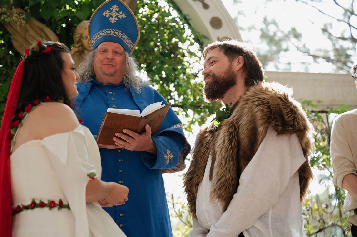 Medieval wedding ceremony with officiator reading from book under outdoor pavilion.