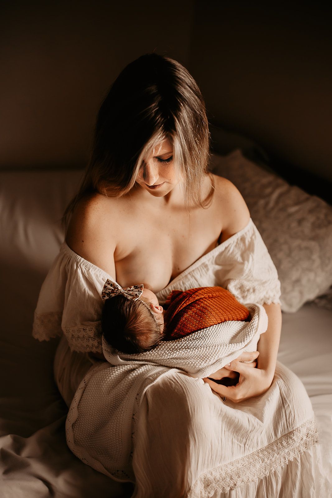 A mother sits on her bed nursing her newborn baby girl.