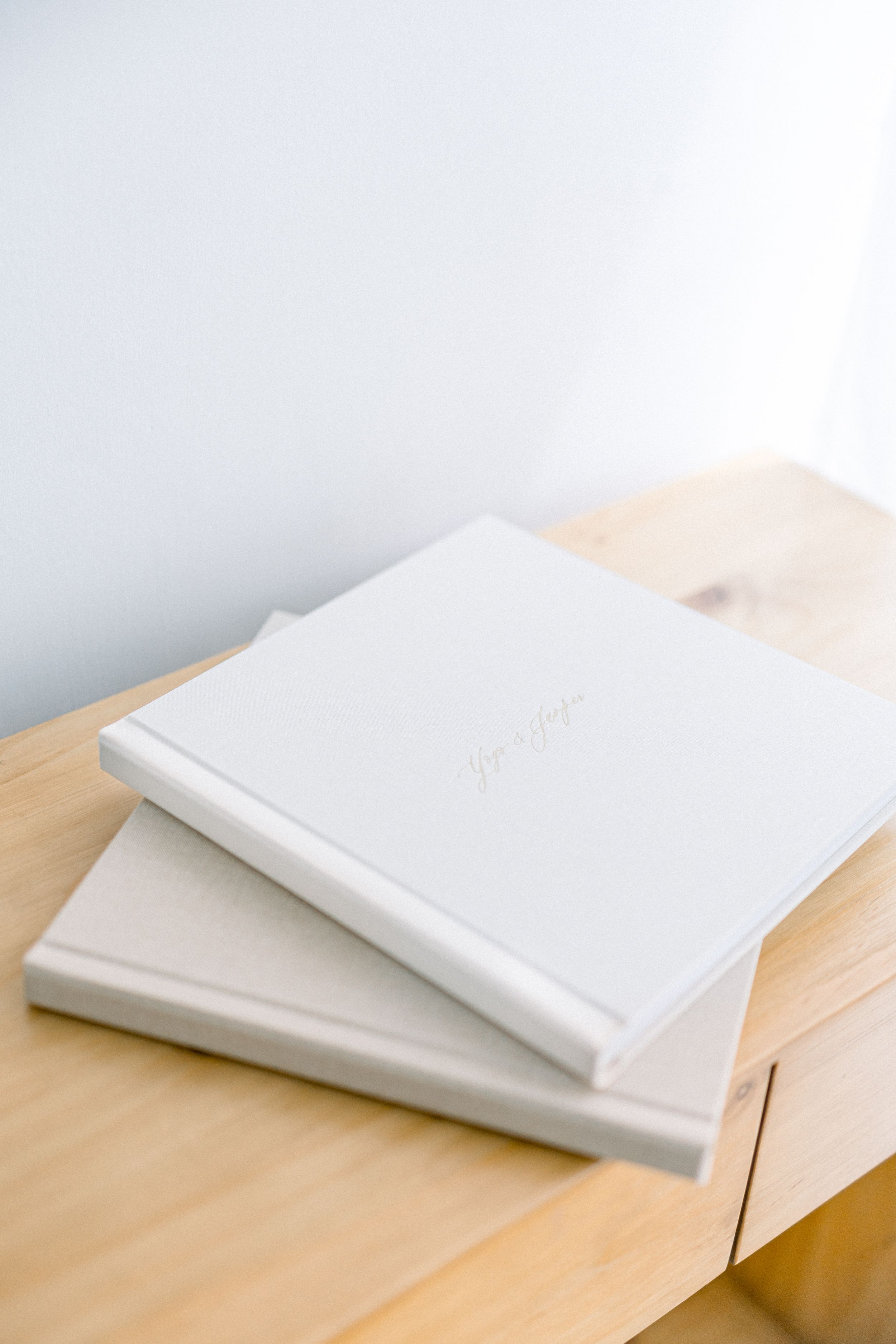 Two white wedding albums stacked on a wooden surface in minimalist style.