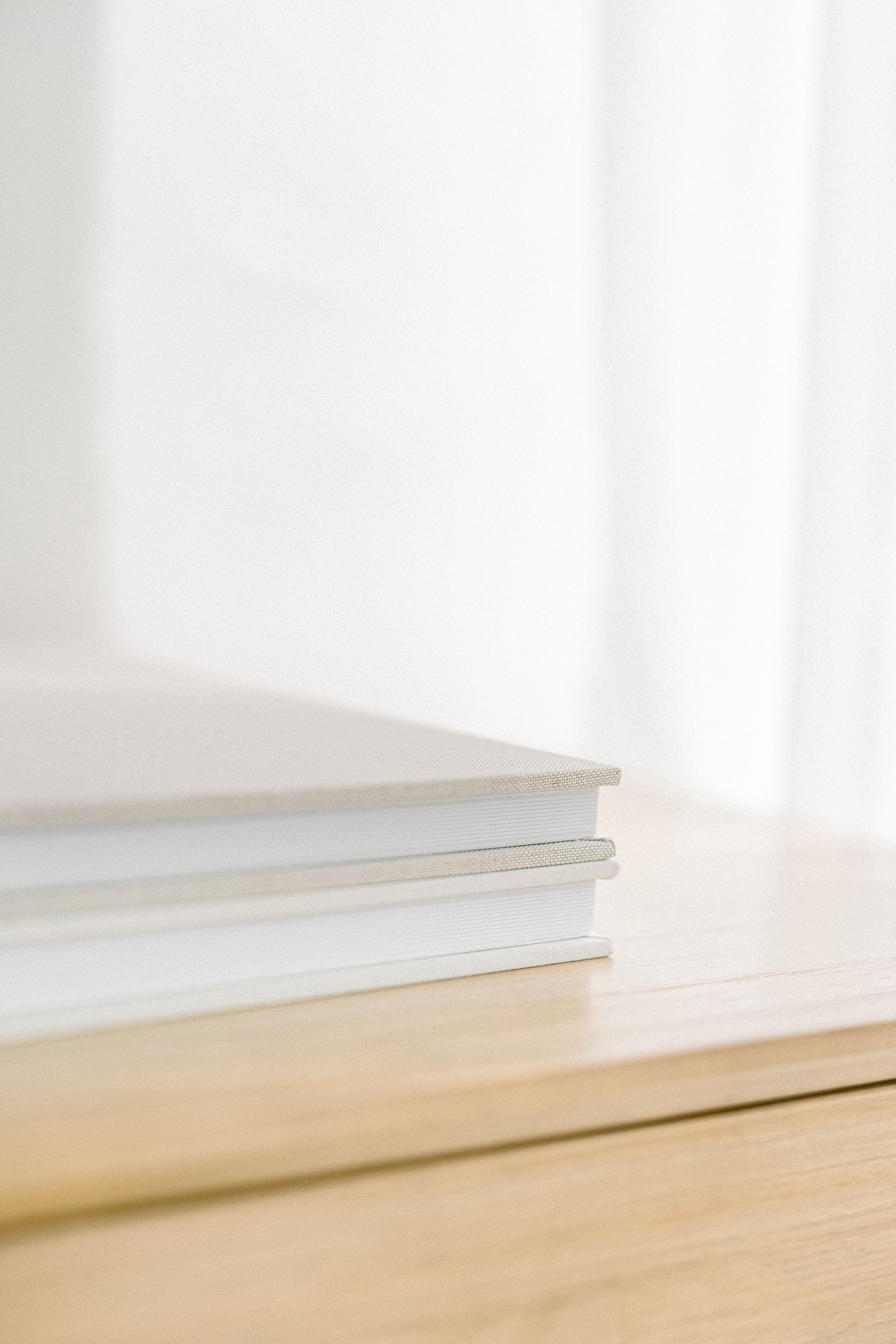 White photo albums stacked on wooden table with soft natural lighting.
