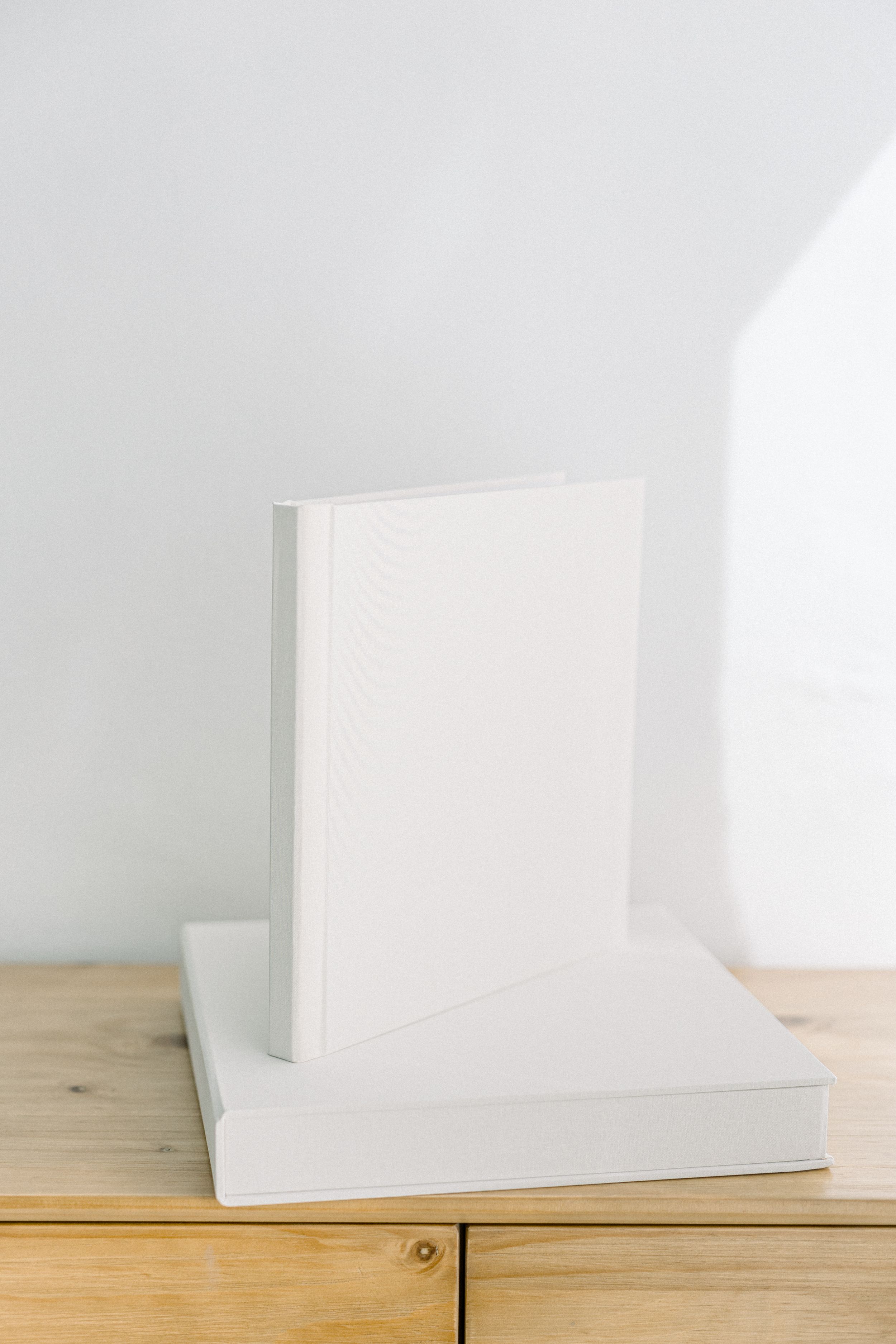 Minimalist white books or albums arranged on wooden surface against white wall.