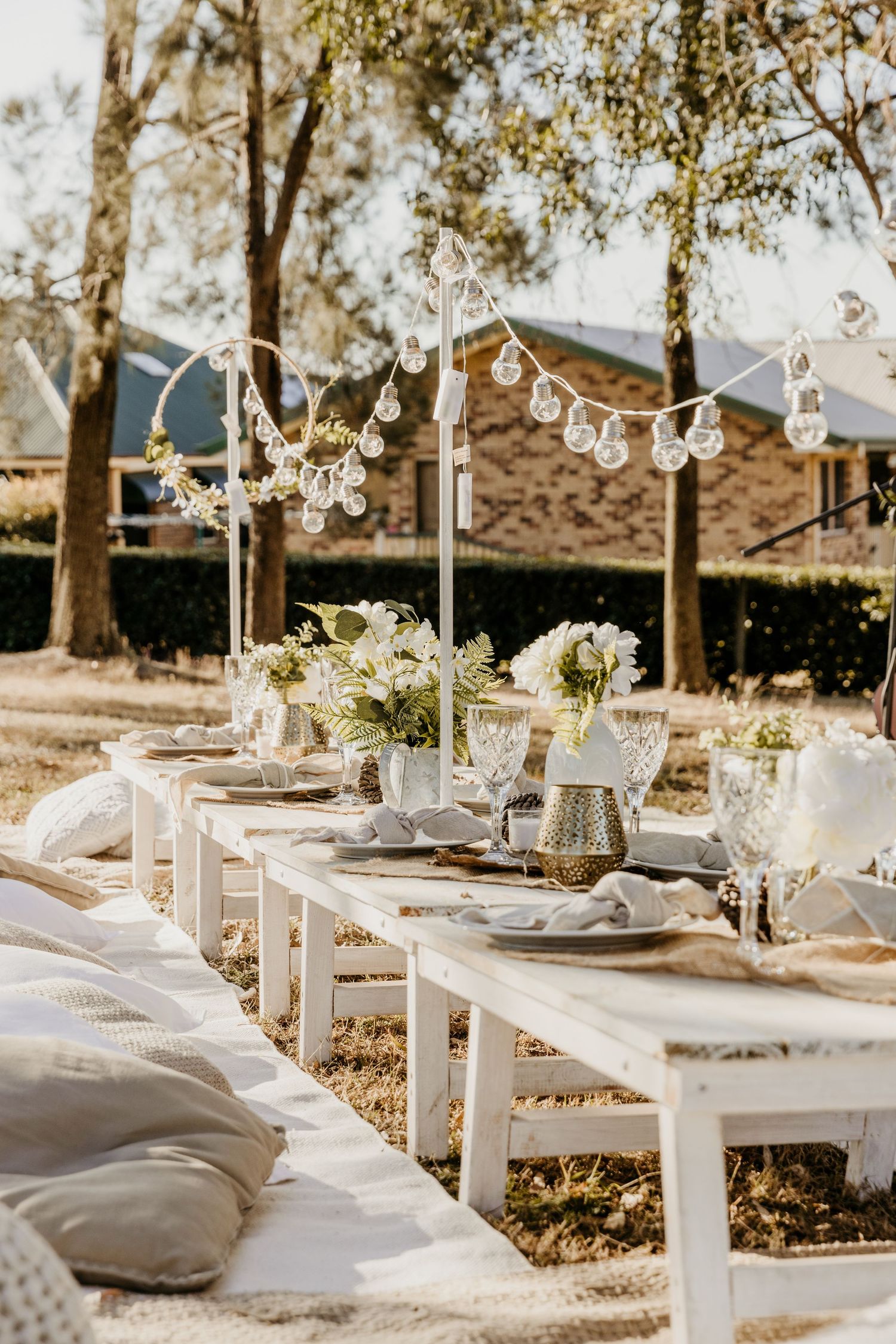 Elegant outdoor dining table set with white linens and hanging string lights.