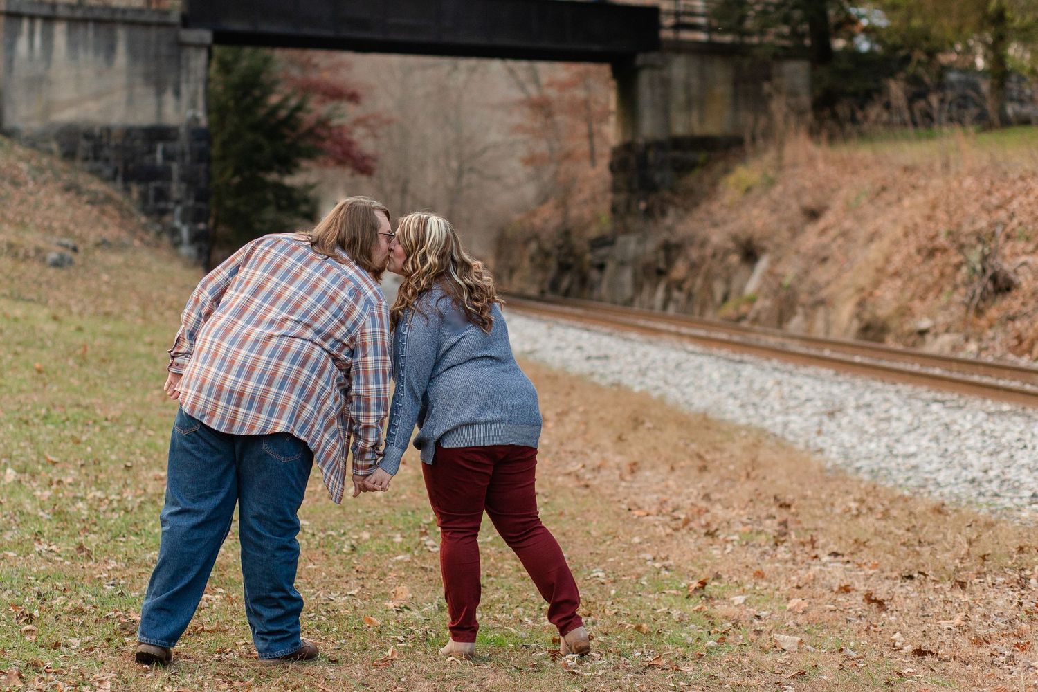 A couple leans together while walking along railroad tracks on an autumn day.