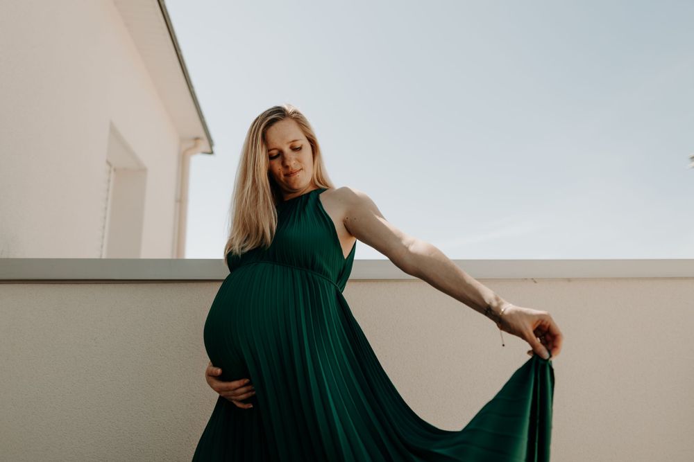 A pregnant woman in an emerald green dress poses dramatically against a light background.