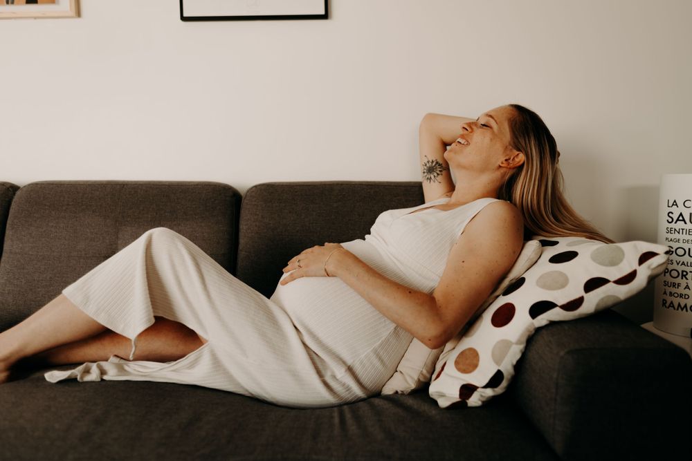 A pregnant woman rests comfortably on a grey couch with polka dot pillows.