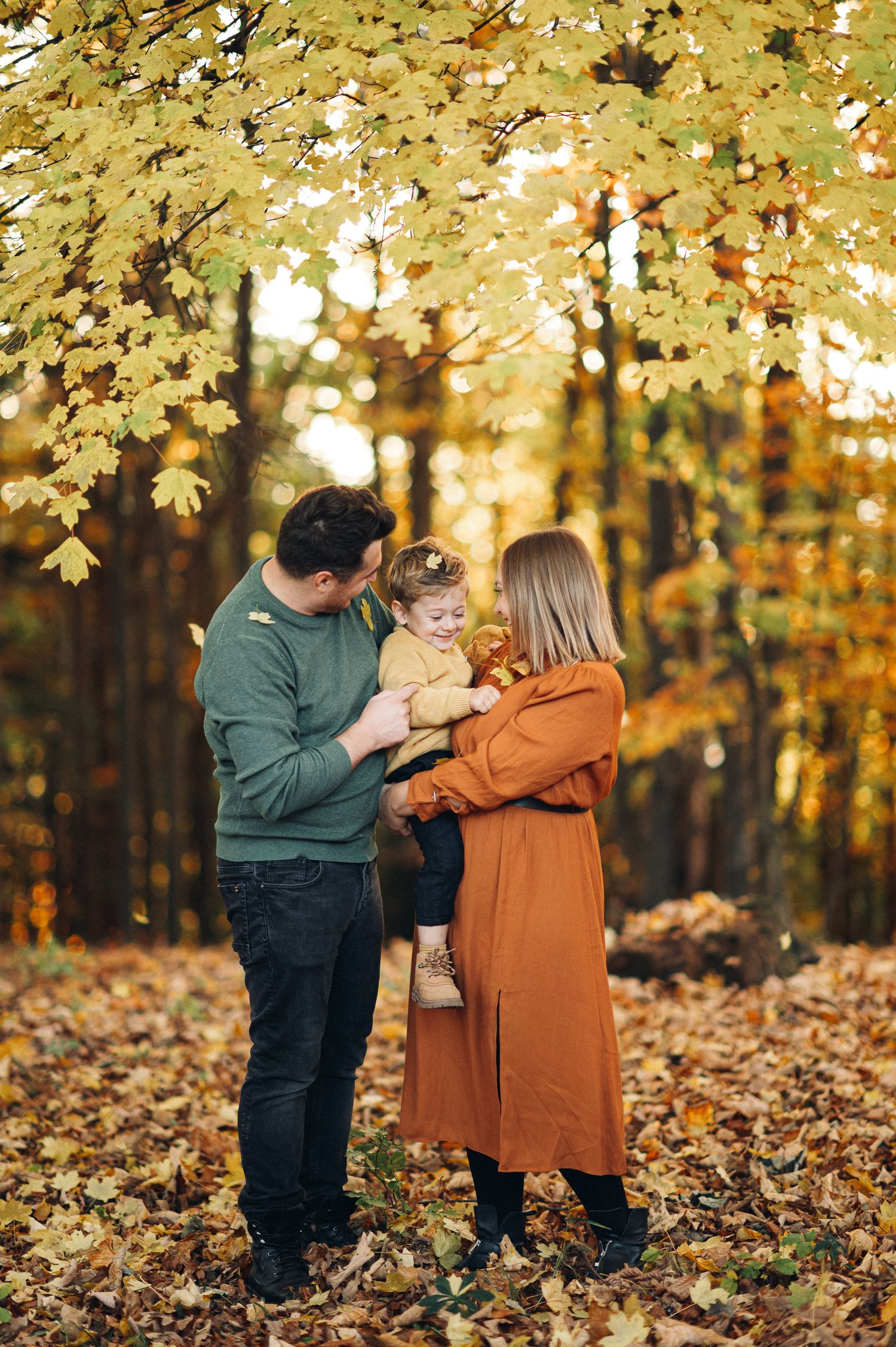 Family enjoying autumn scenery under golden maple trees in casual fall attire.
