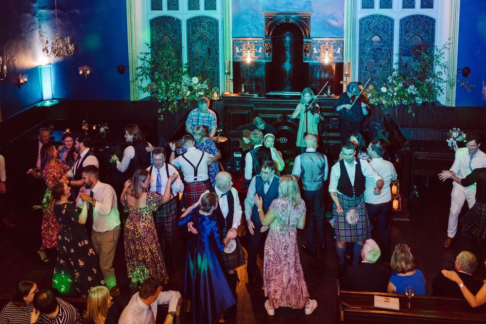 Wedding guests dancing and celebrating on a dimly lit dance floor with blue lighting in the background.