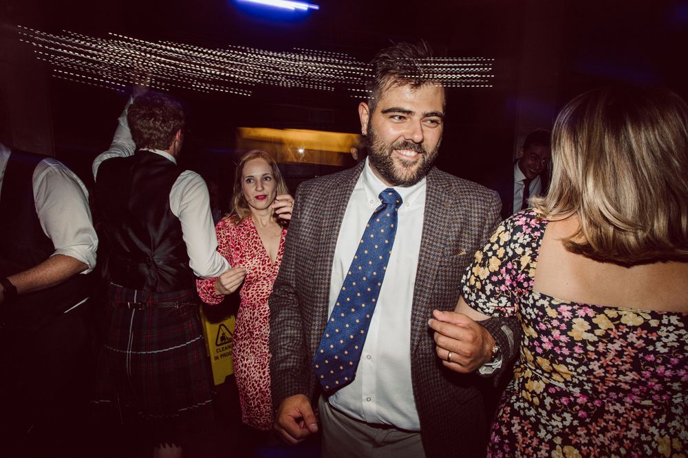 Wedding guests dancing and laughing together under decorative string lights.