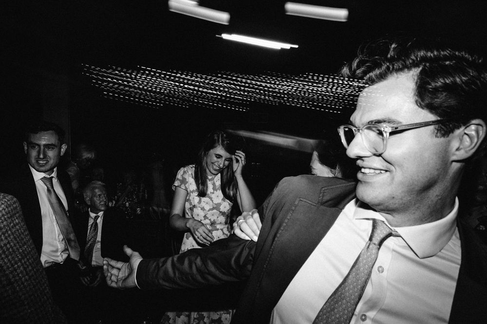 Black and white photo of guests enjoying themselves at a dimly lit wedding reception.