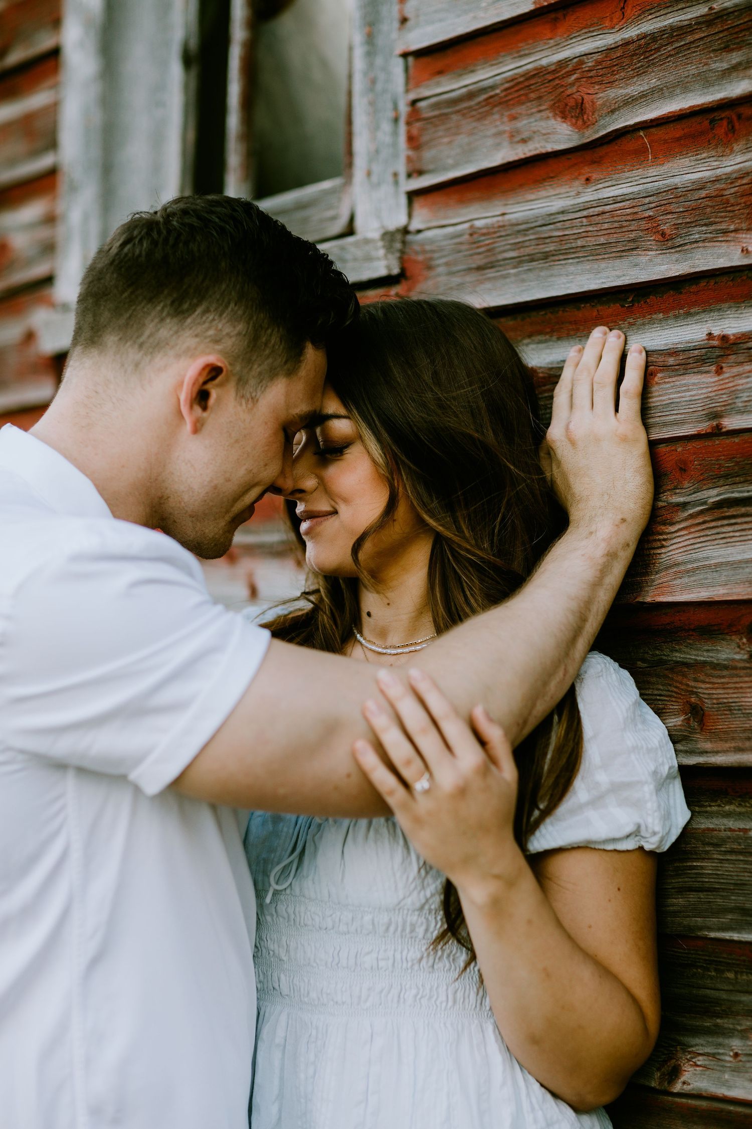 A romantic couple embraces against a rustic wooden wall during a photoshoot.
