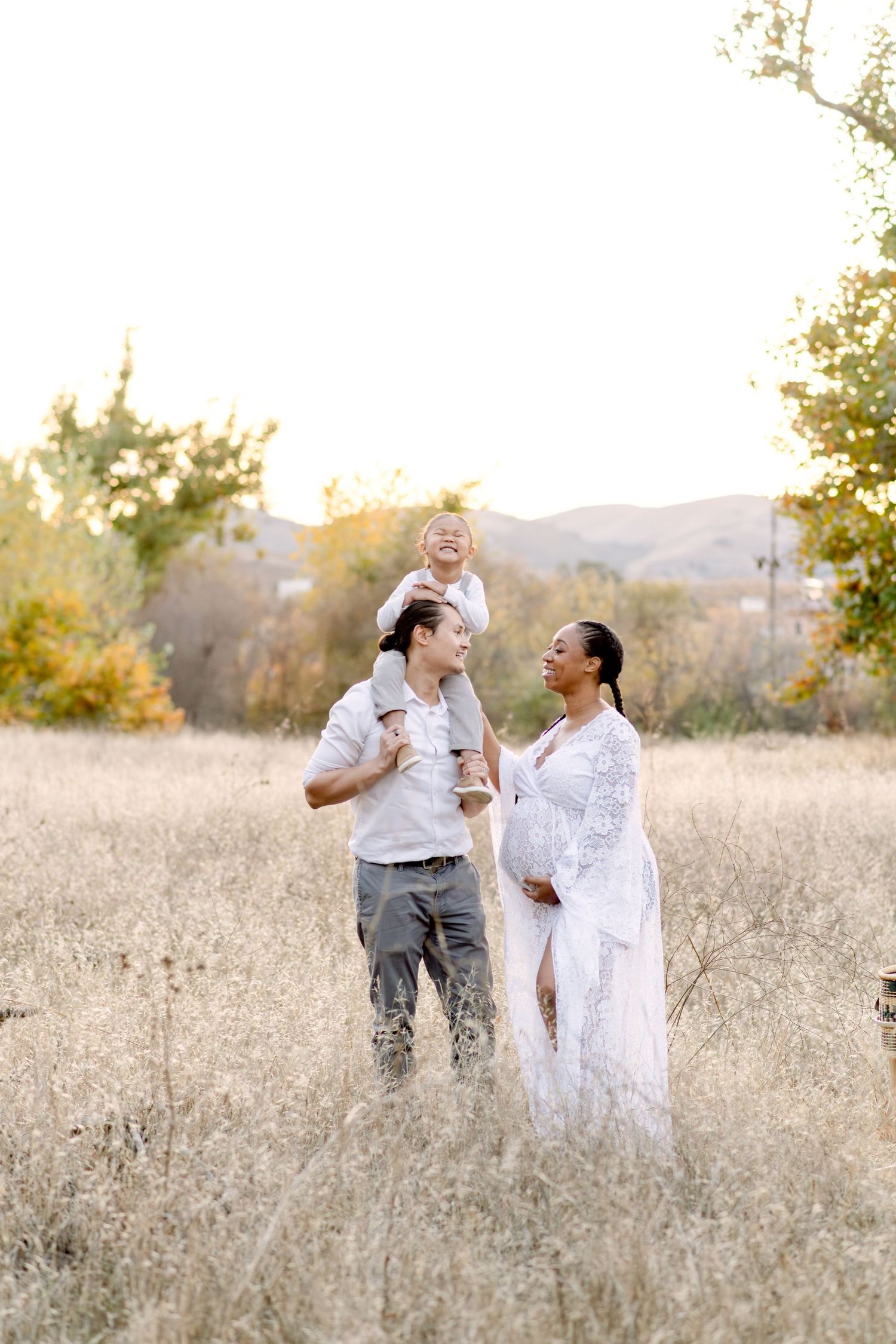 A playful family moment photographed in a golden field with mountains and autumn trees in the background.