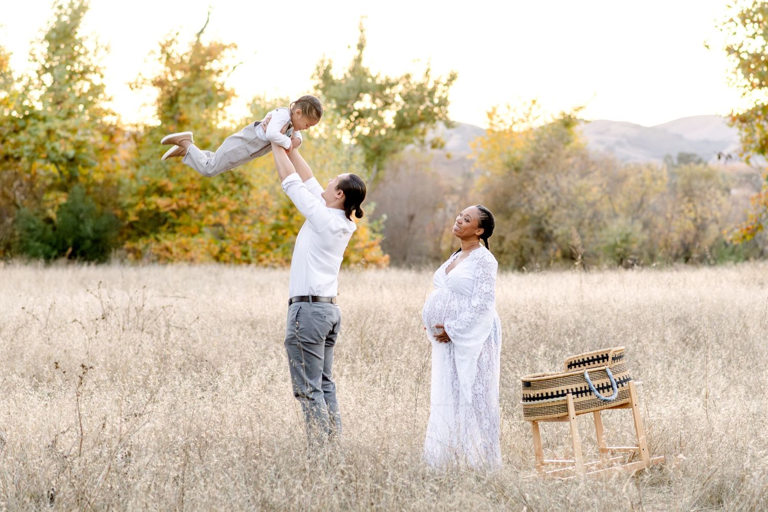 A joyful family plays together in a field during golden hour with mountains visible in the distance.