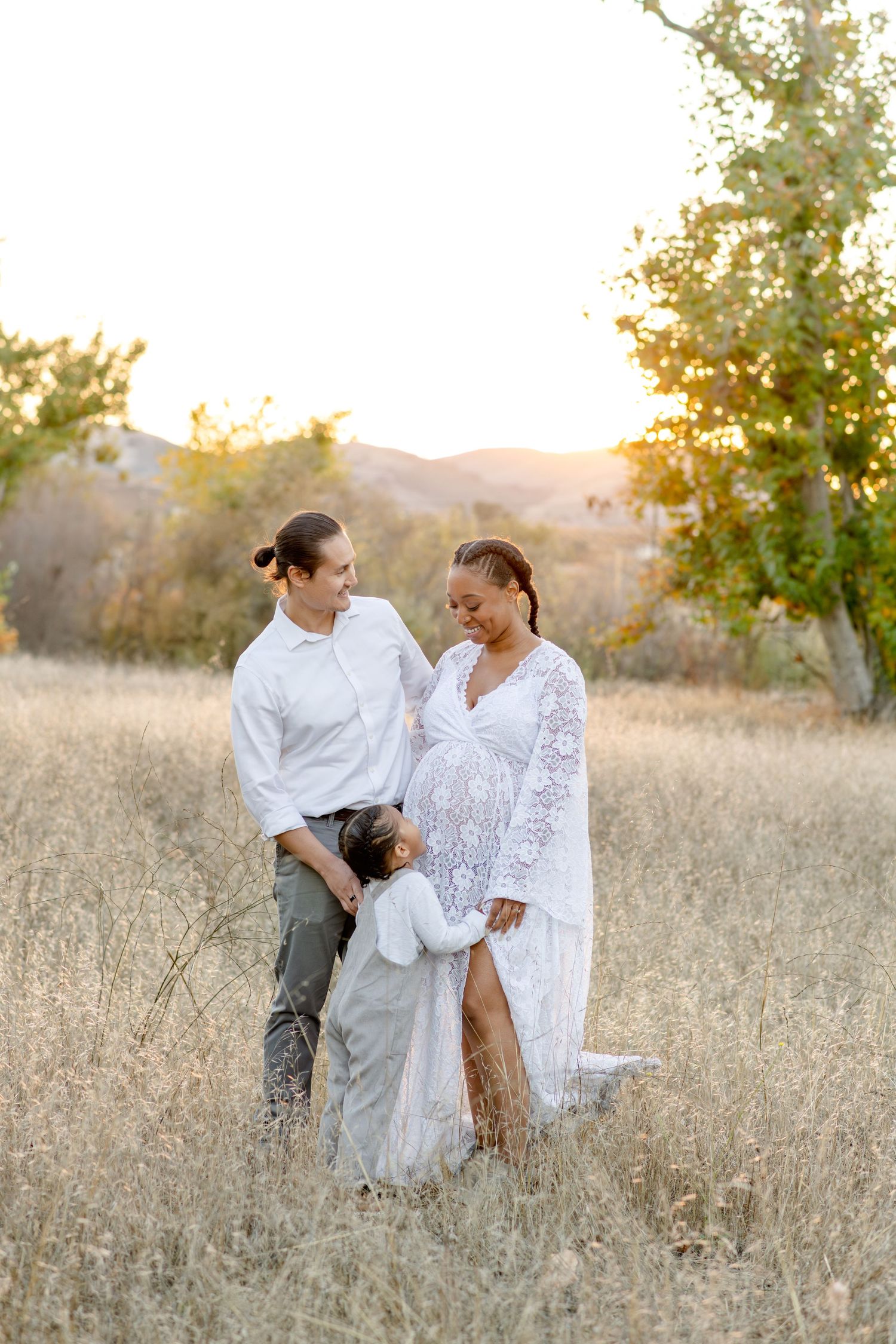 Family maternity portrait in golden field at sunset showing intimate moment together.