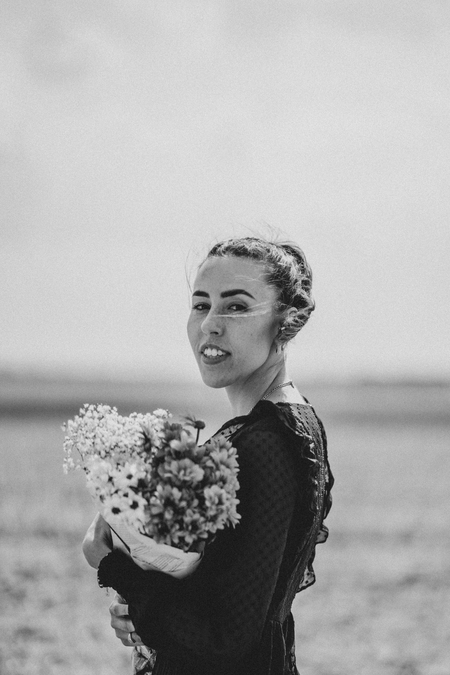 A black and white portrait of someone holding flowers in a field.