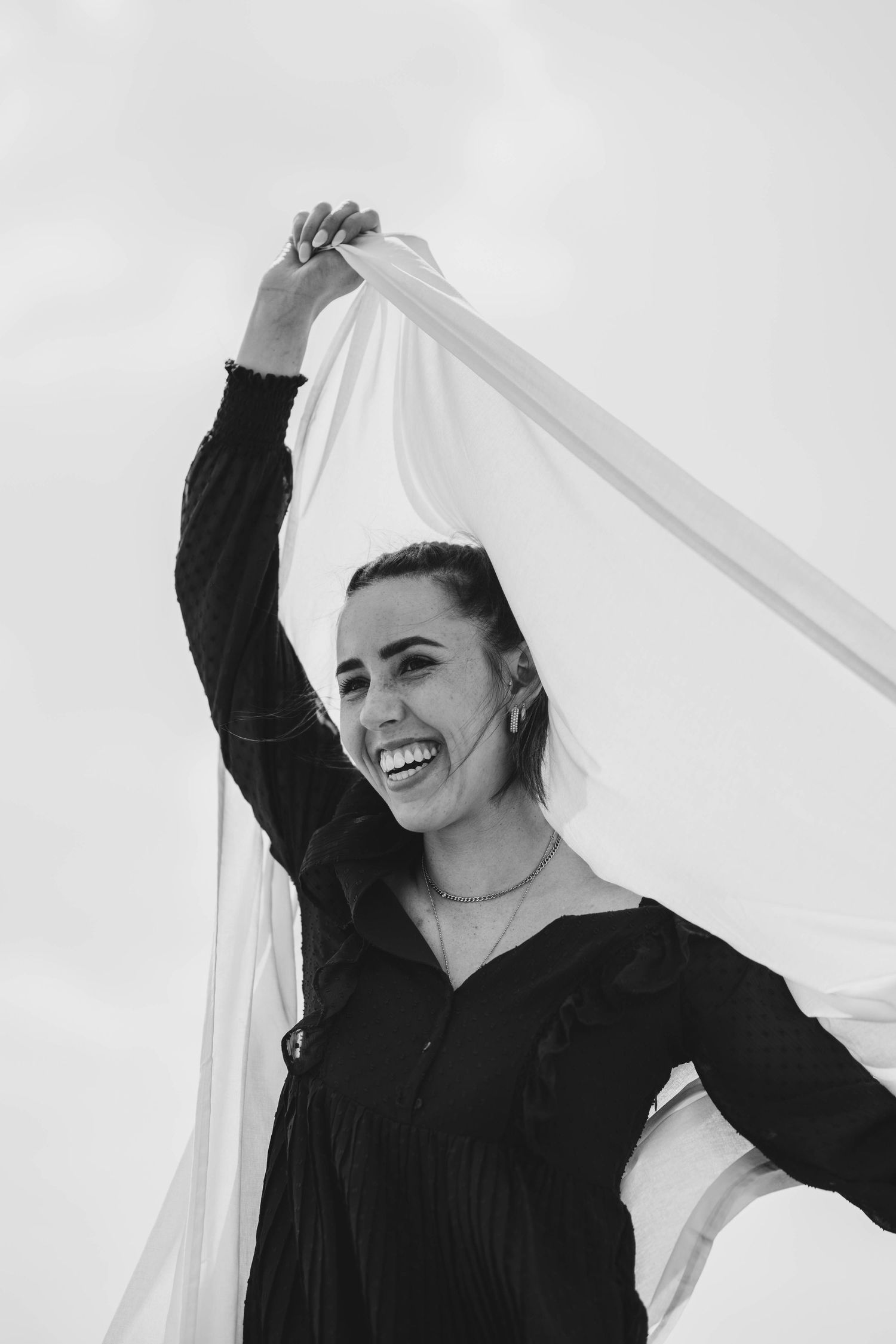 A black and white photo of someone joyfully holding flowing fabric overhead.