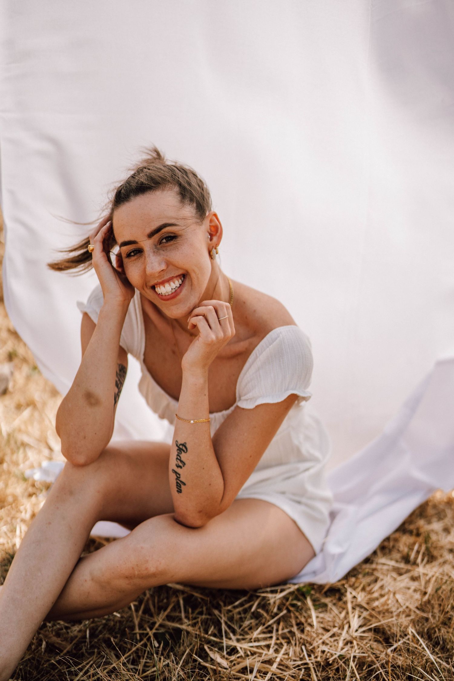 A casual portrait of someone sitting on hay in a white summer dress.
