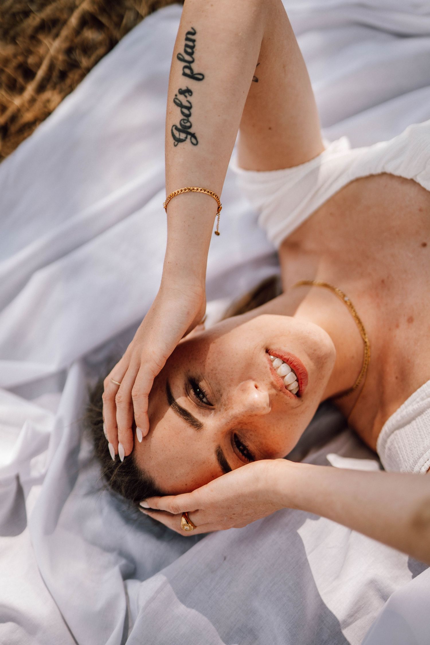 A person lying on white fabric outdoors with a visible tattoo on their arm.