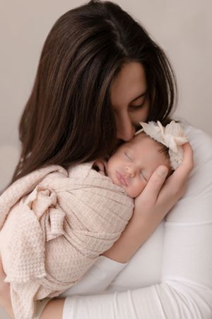 Tender moment captured between parent and sleeping newborn wrapped in soft beige swaddle.