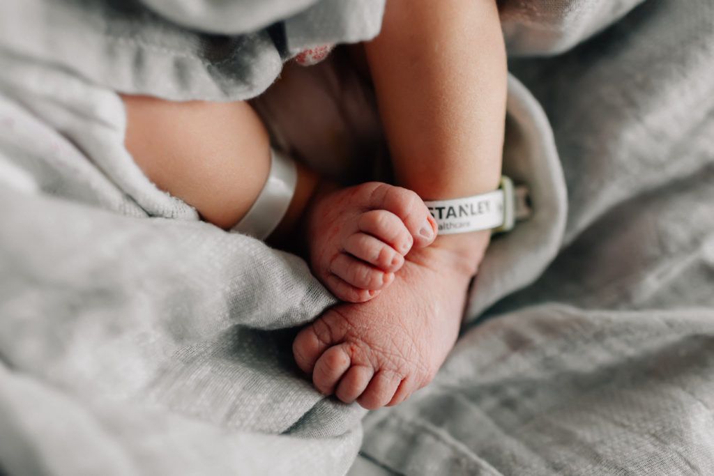 Close-up of tiny newborn feet wrapped in a soft gray blanket with hospital ID band.