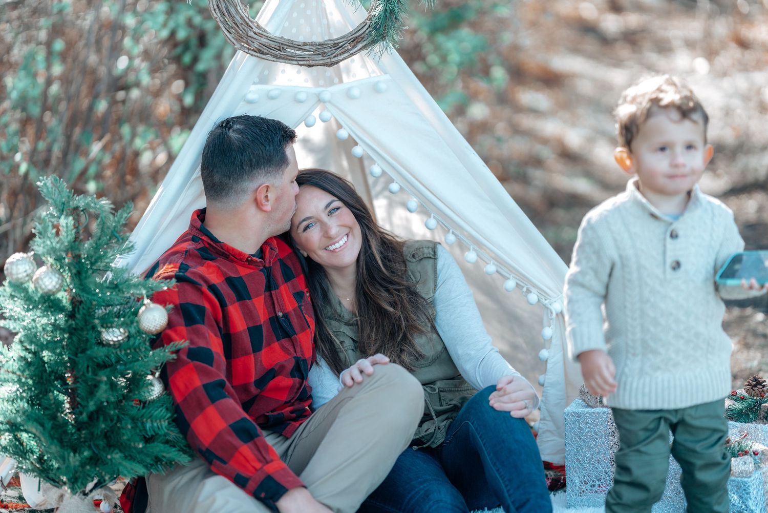 Family posing together near a decorative white teepee and small Christmas tree.