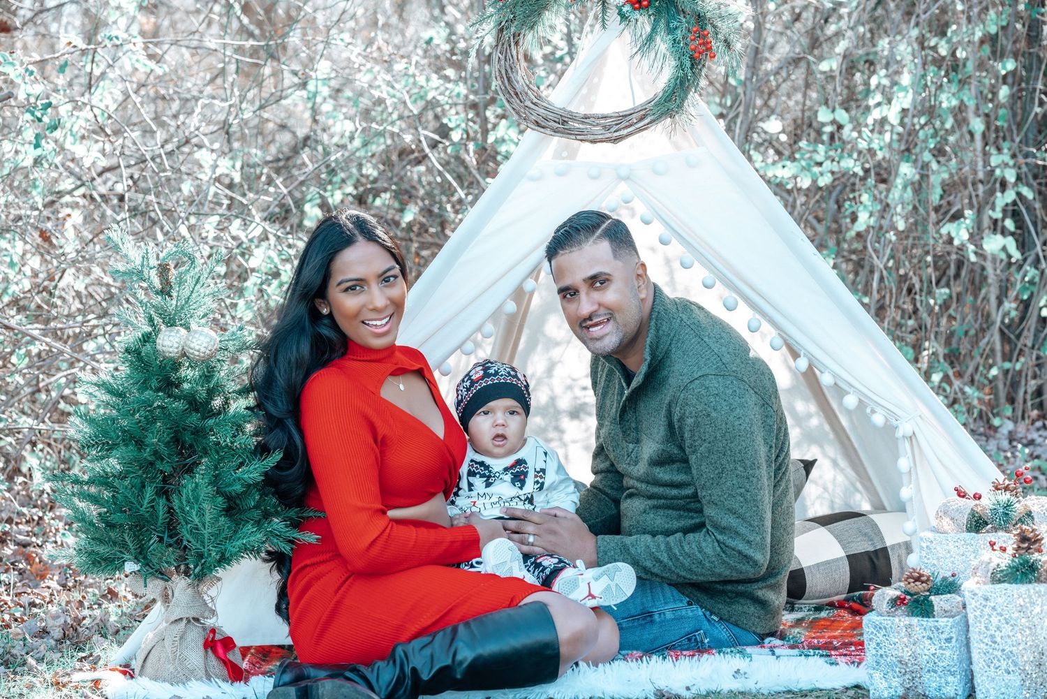 A family sits together on a blanket near a white teepee tent during a winter photo session.