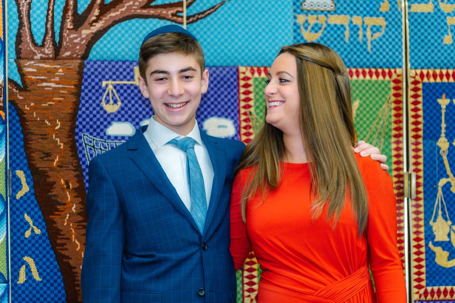 A formal portrait against a decorative Jewish-themed mural background.
